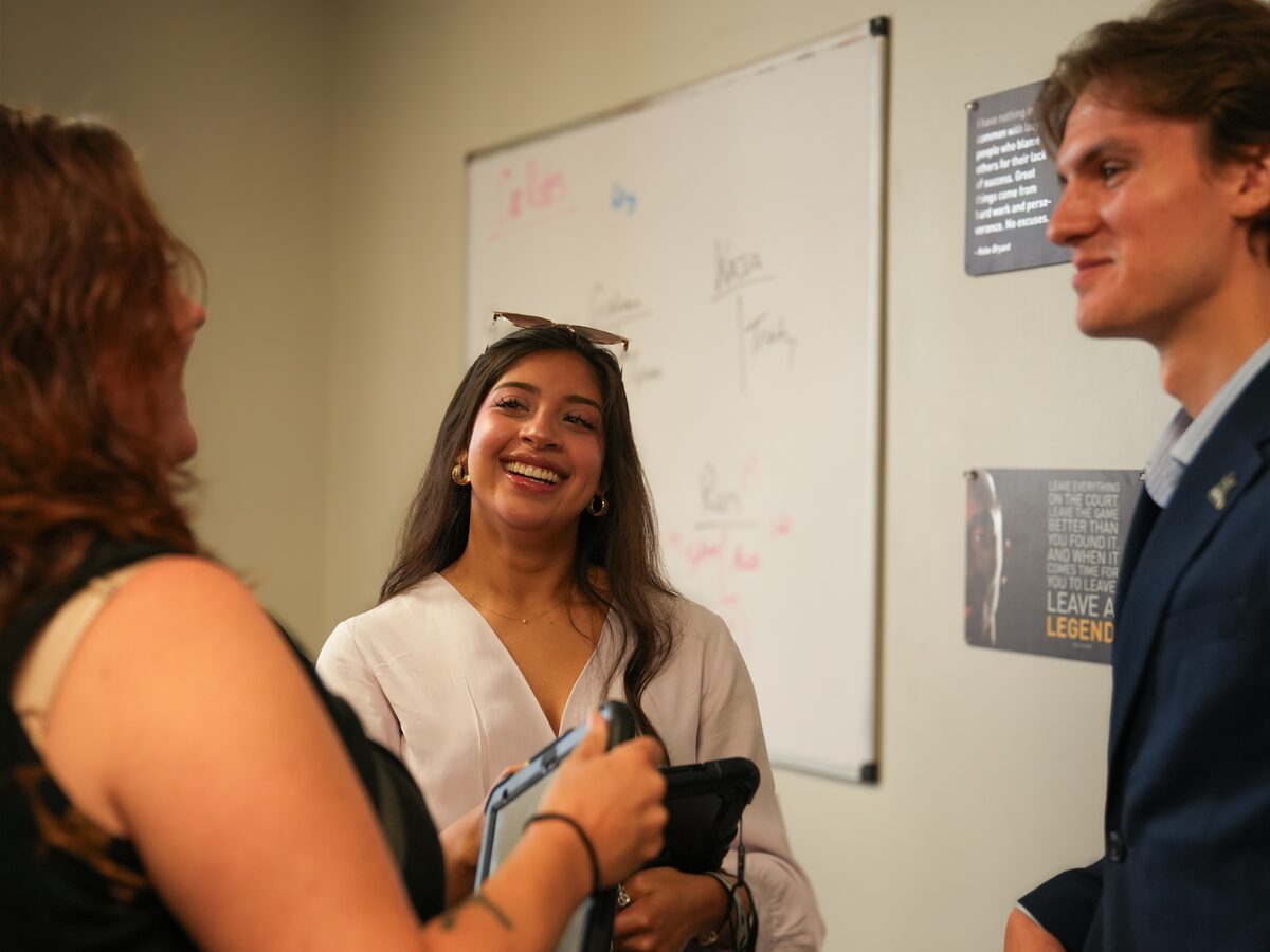 Three Coast to Coast Events team members talking and laughing together in the office in front of a whiteboard