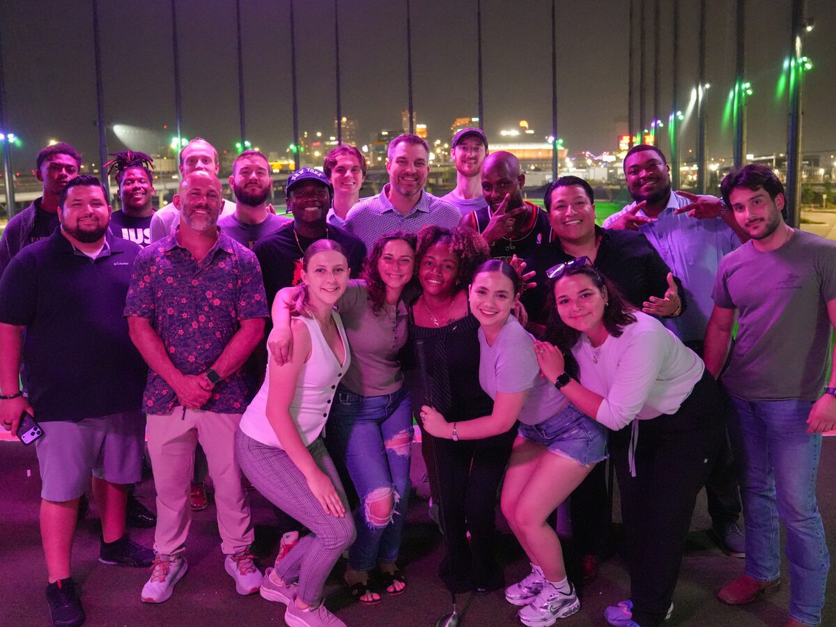 The Coast to Coast Events team gathered together for a group photo at an evening team outing, with a lit city skyline behind them